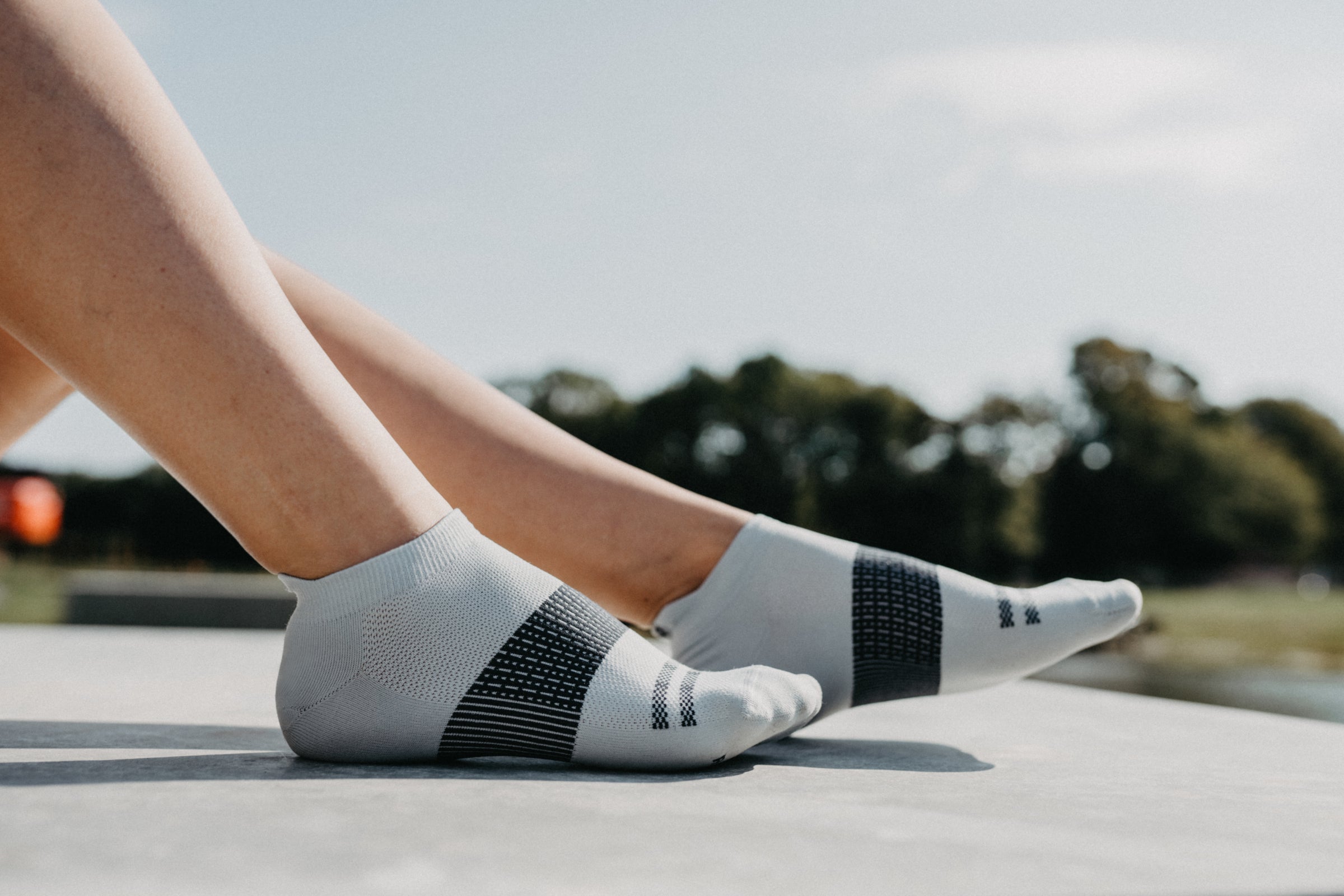 A person's lower legs and feet wearing Rockay Accelerate socks, positioned side by side on a concrete surface outdoors