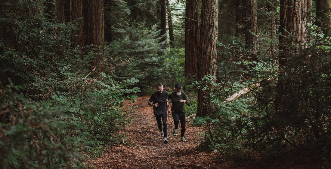 Two men trail running through a forest wearing Rockay gear