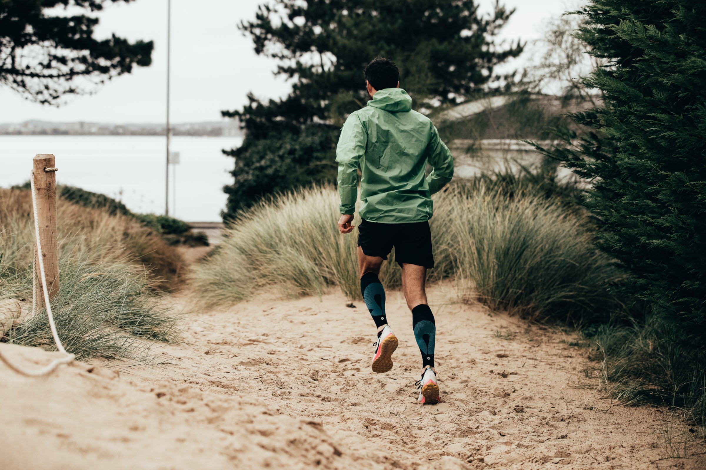 Runner wearing Rockay Blaze compression calf sleeves while jogging along a sandy beach path