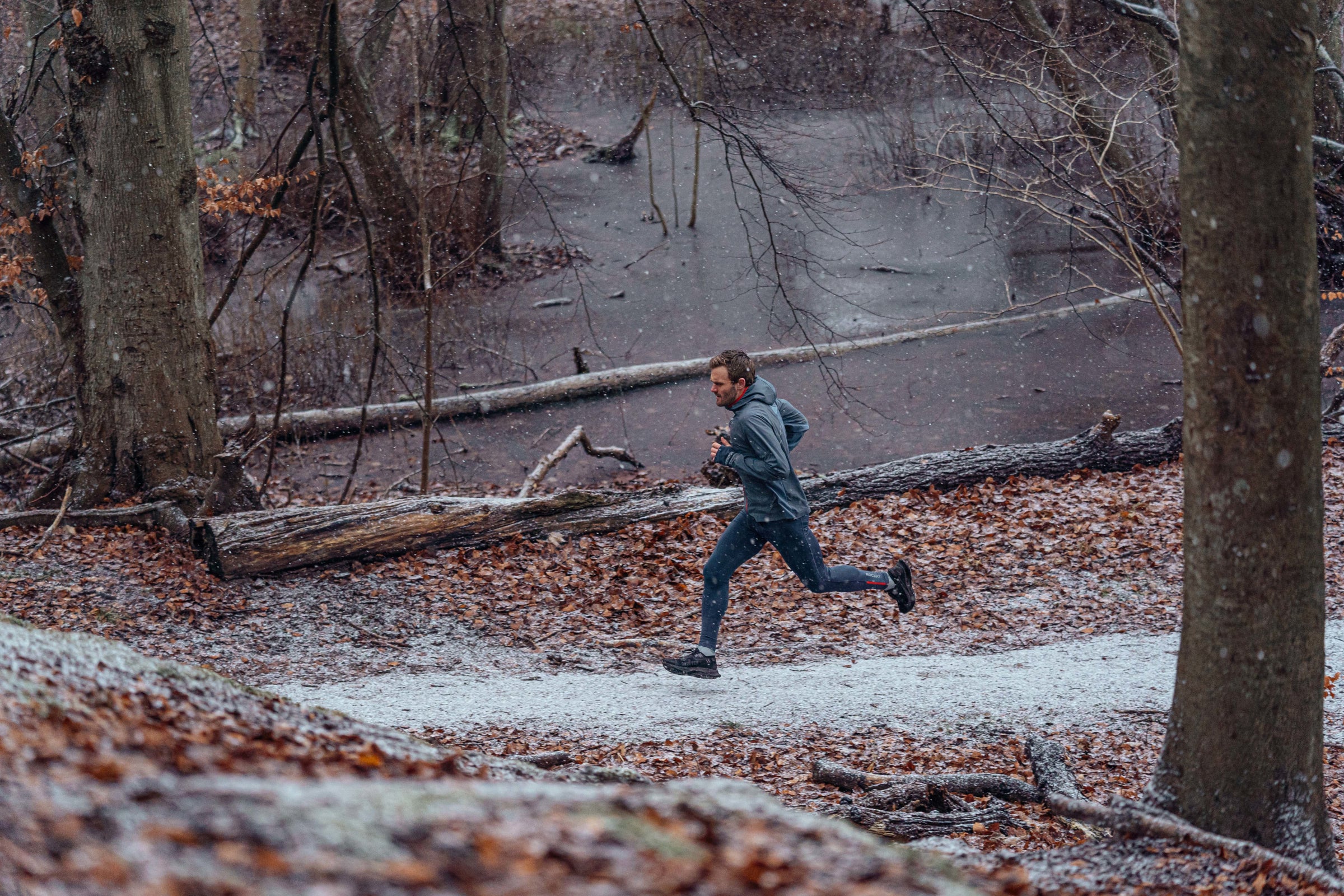 Man running through a snowy forest trail