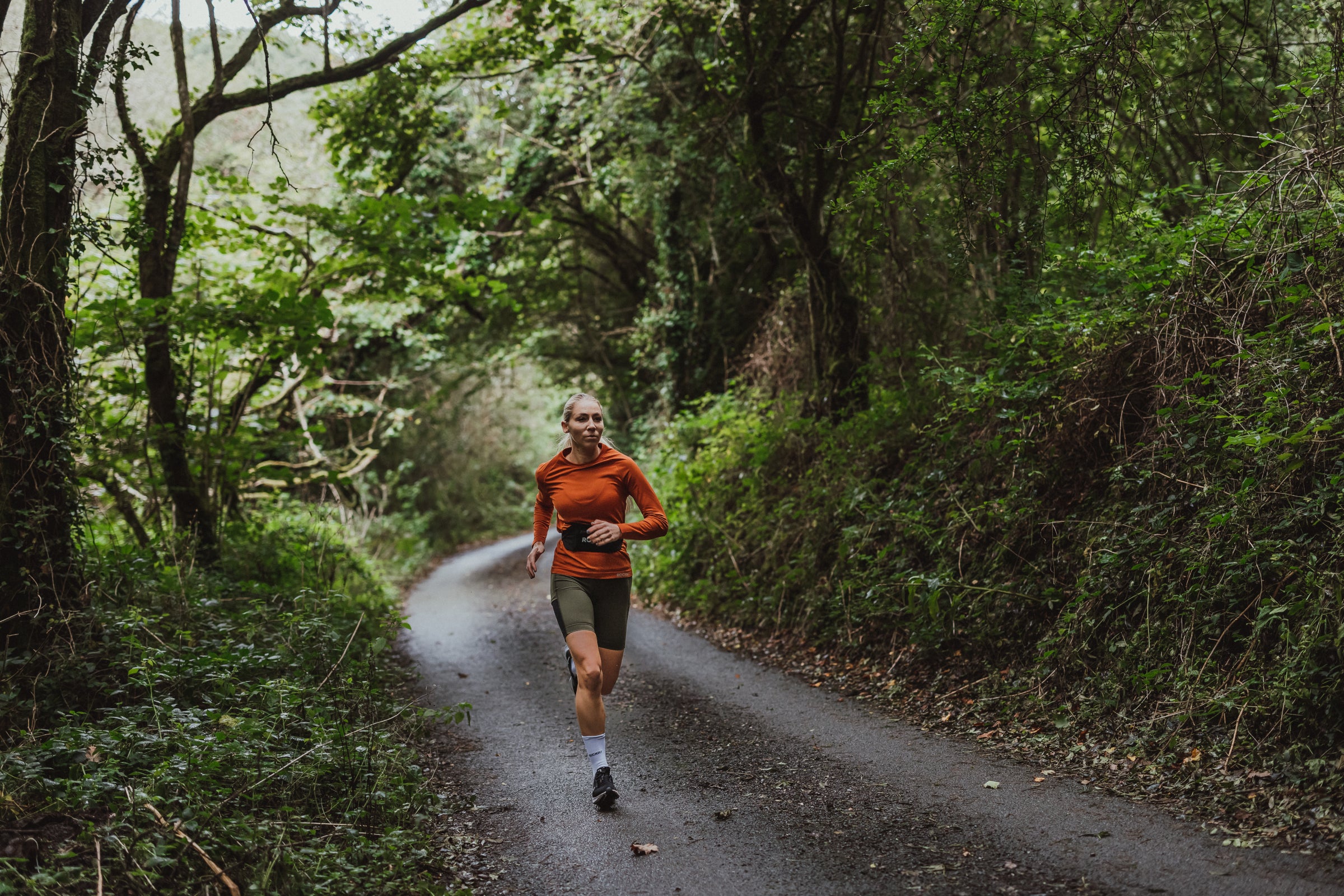 Woman trail running in Rockay gear through a lush forest path
